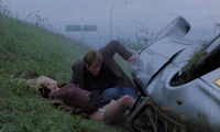 a man and woman lying on the ground next to a car